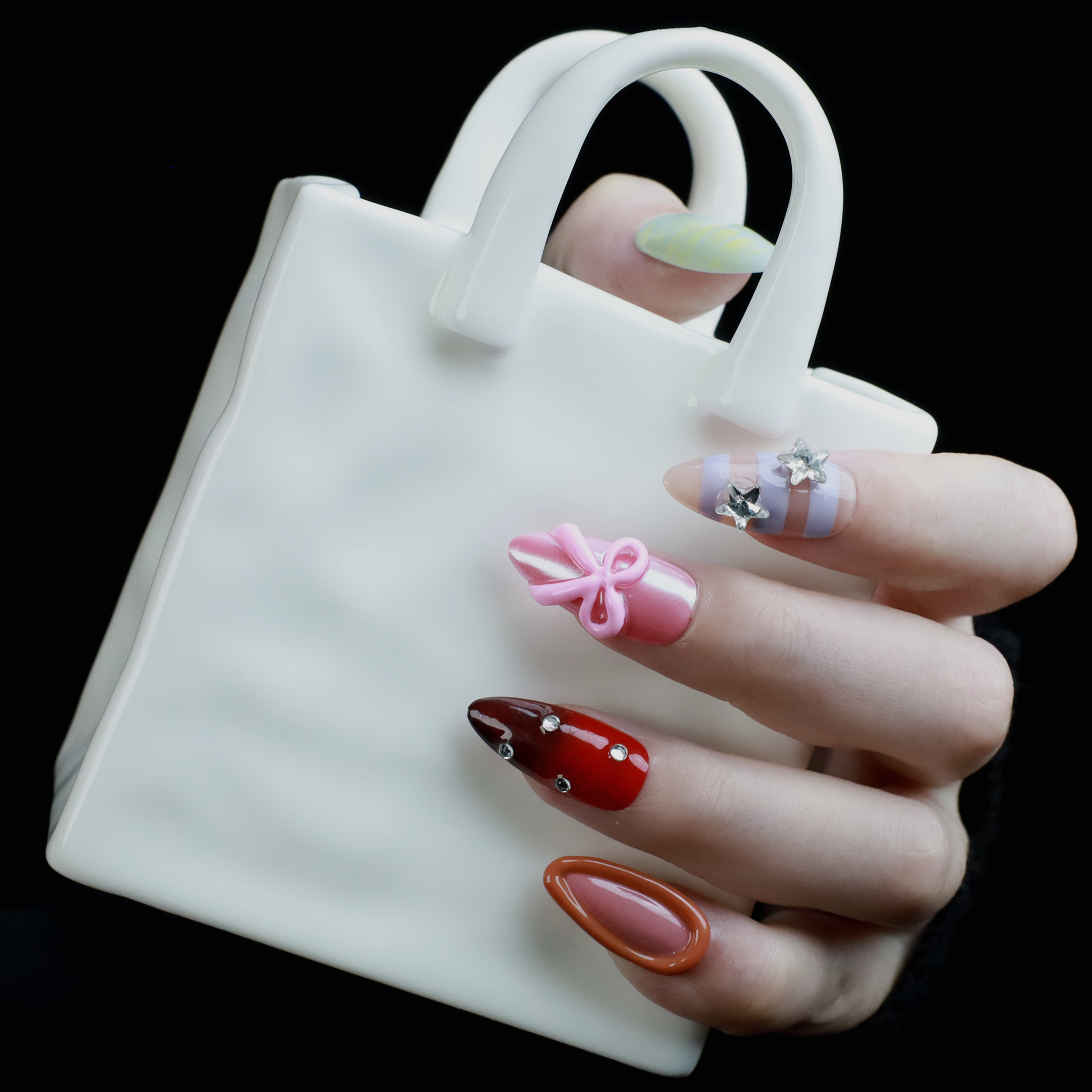 A hand with We Do Nails Candyland Dream Press-On Nails displays playful designs. Features include pastel yellow plaid, clear nails with bows and rhinestones, pink nails with a bow, shiny red with rhinestones, and glossy rust-orange—all set against a dark backdrop.