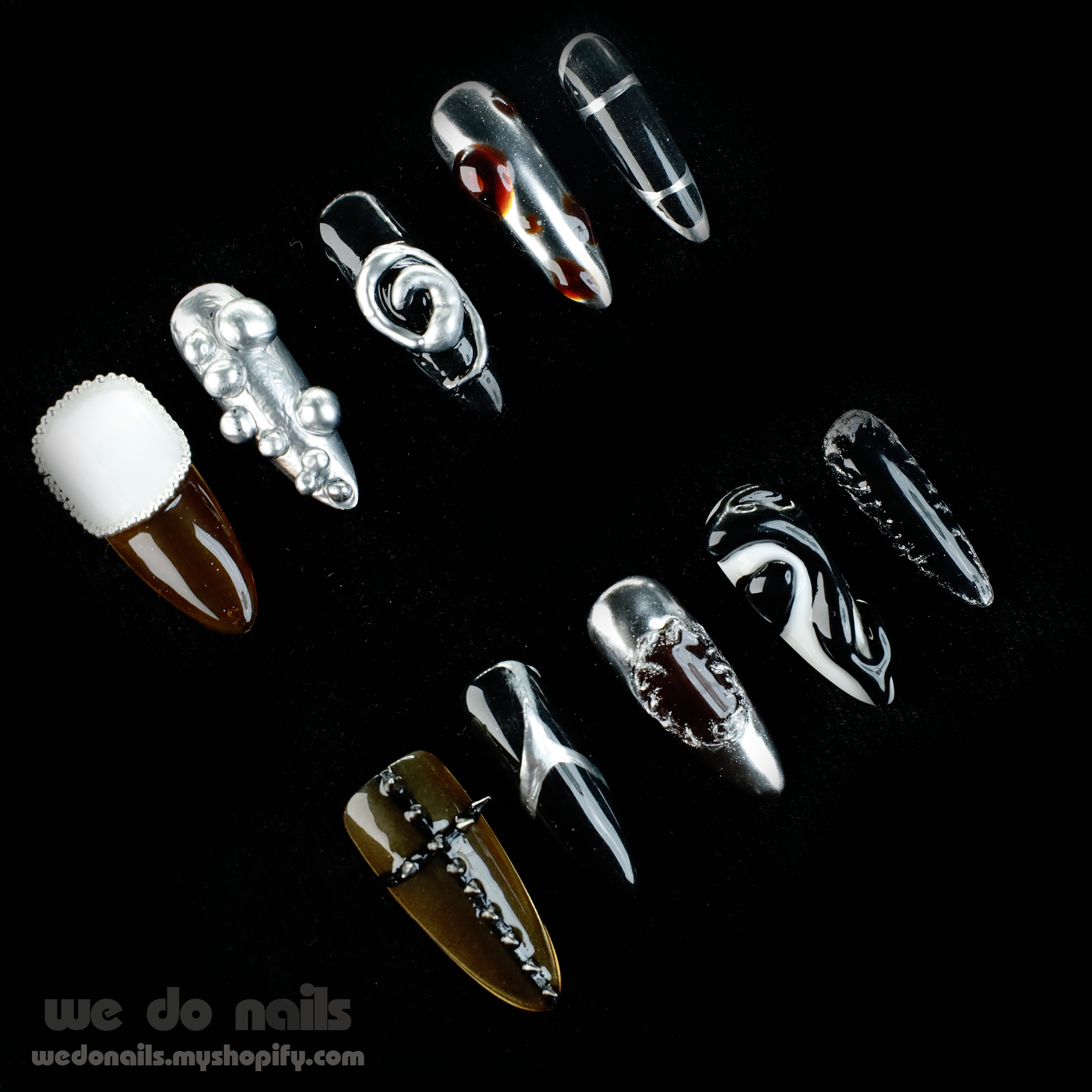 A hand holds a white mug, featuring long, intricately designed black and white Cool Rock Press-On Nails by We Do Nails from the Futuristic Noir Collection, adorned with metallic and gem accents against a dark background—an embodiment of avant-garde flair.