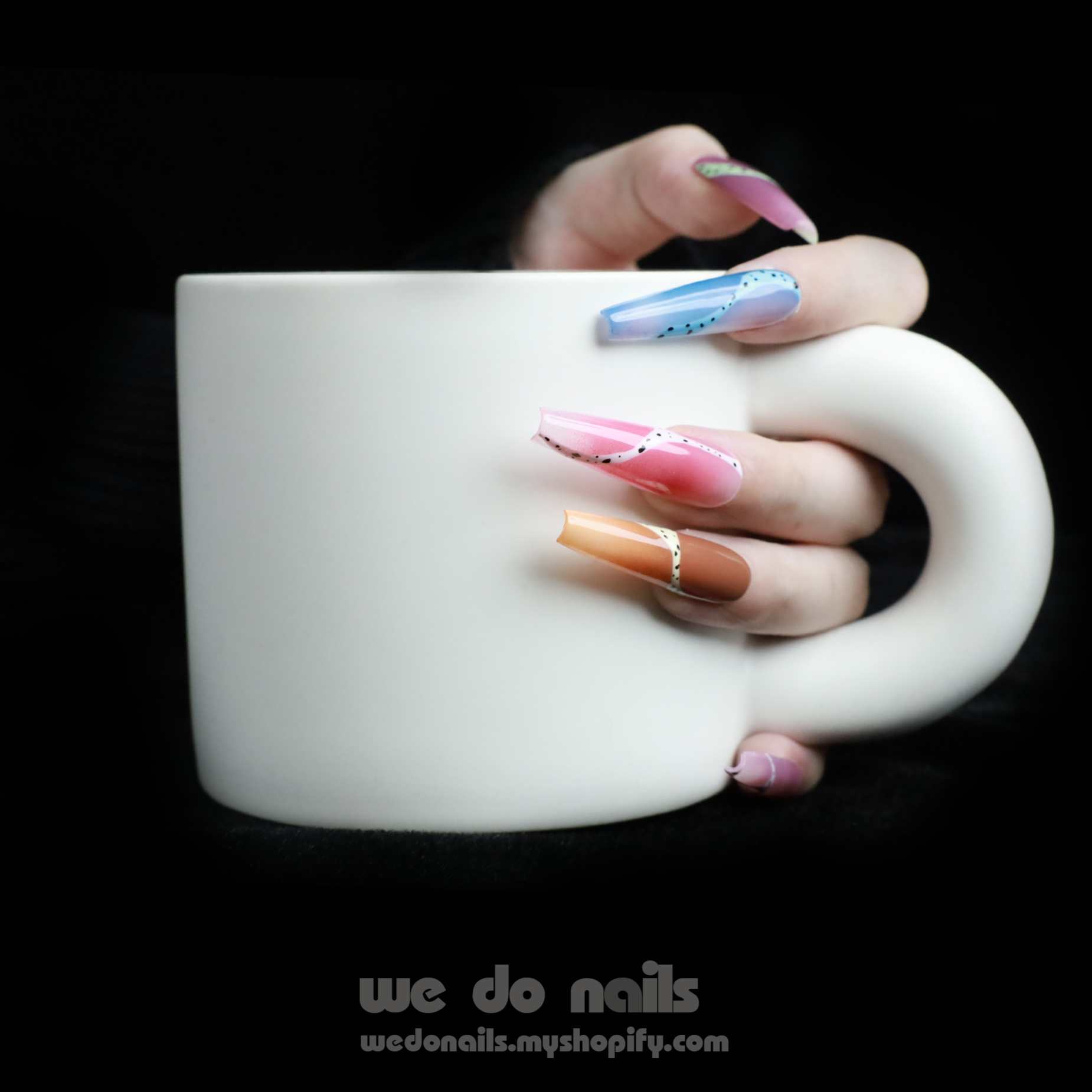A hand adorned with Milky Rainbow Press-On Nails exhibits a smooth gradient and dotted 3D designs against a black background. The text We Do Nails appears alongside the website link, emphasizing the brands artistry.