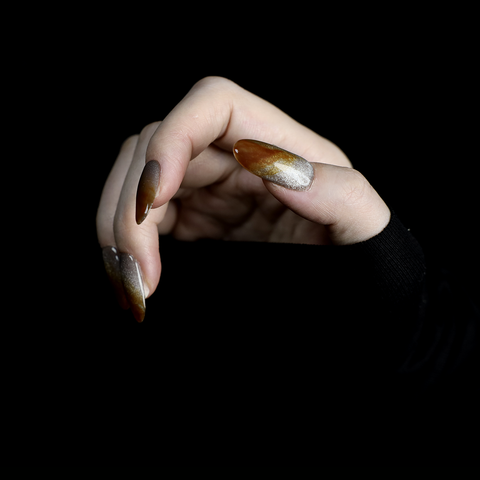 A hand with We Do Nails Elegant Brown Marble Press-On Nails, featuring a subtle metallic chrome accent, holds a simple white mug against a black backdrop.