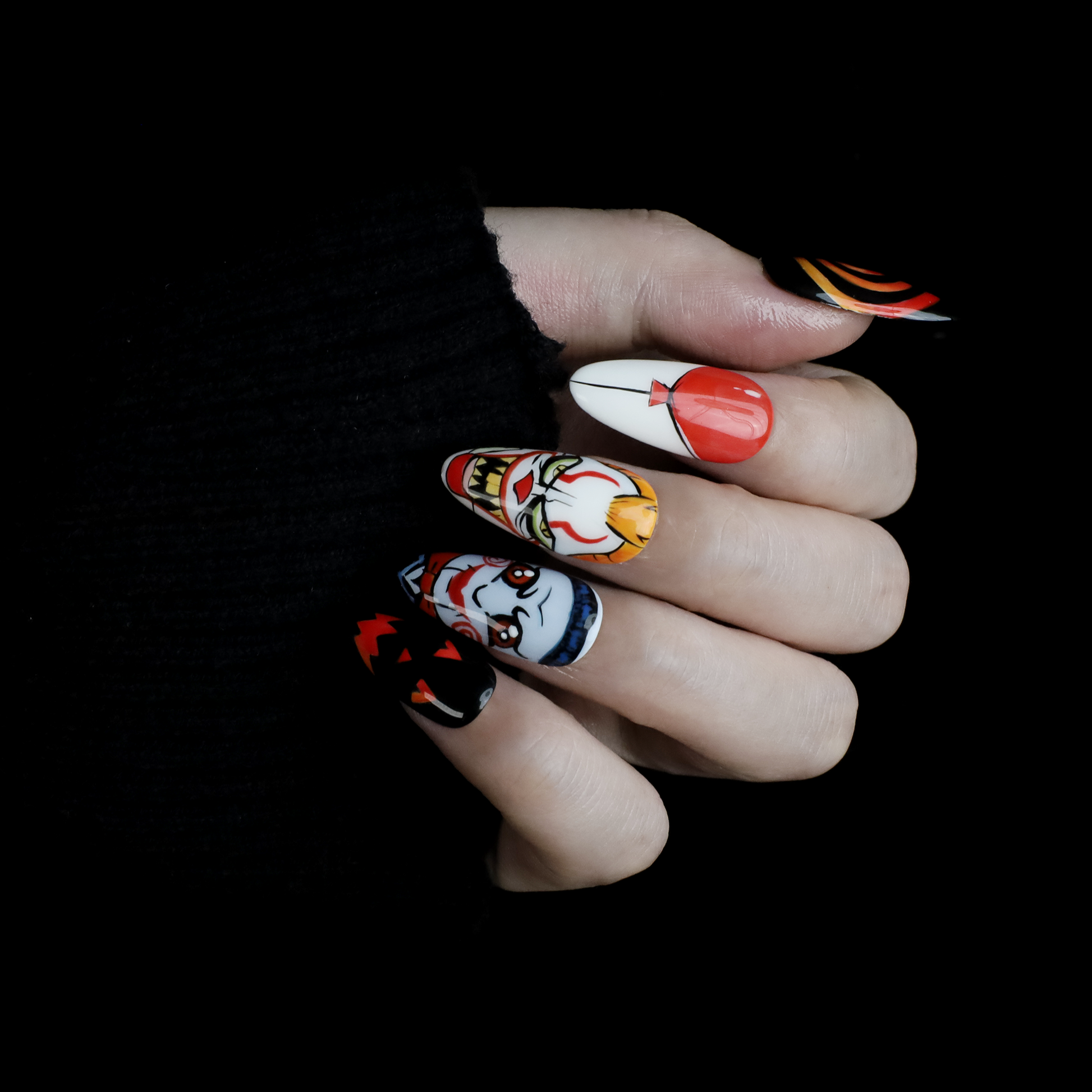 A close-up of two hands shows off the eerie Spooky Nightmares Halloween Press-On Nails by We Do Nails, featuring hand-painted designs like clowns, a pumpkin, and abstract art on a black background while holding a large white mug.