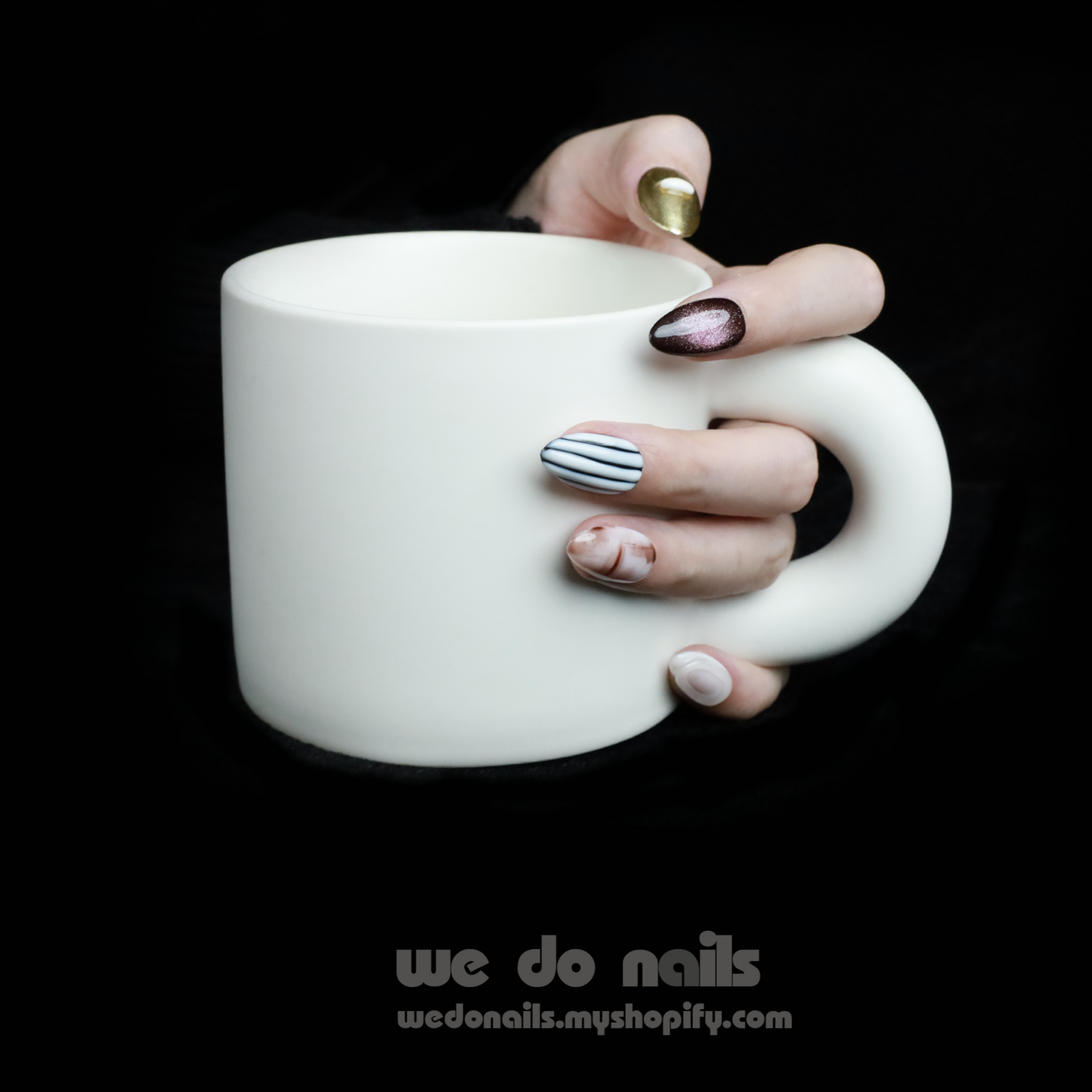 A hand with Elegant Press-On Nails holding a large white mug displays glittery stripes, marbling, and metallic textures with hints of gold. The black background has text: We Do Nails followed by the URL wedonails.myshopify.com.