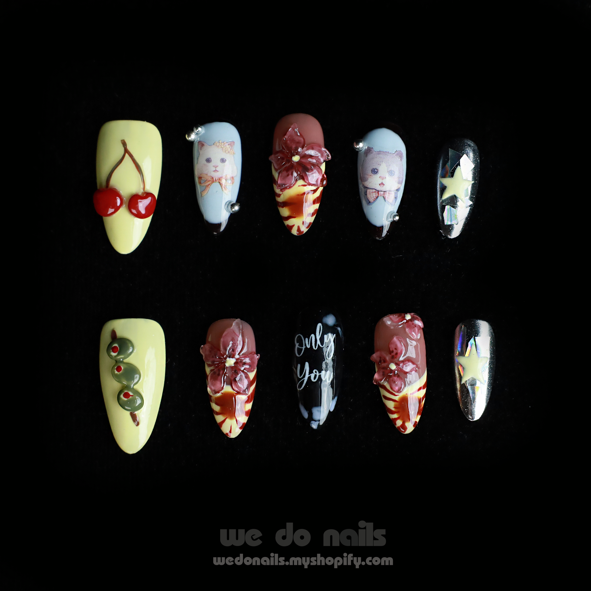 A hand adorned with We Do Nails Extravaganza Press-On Nails, showcasing unique patterns and colors, holds a small white handbag. The dazzling metallics gleam against the black background, highlighting the bold nail art and bag.