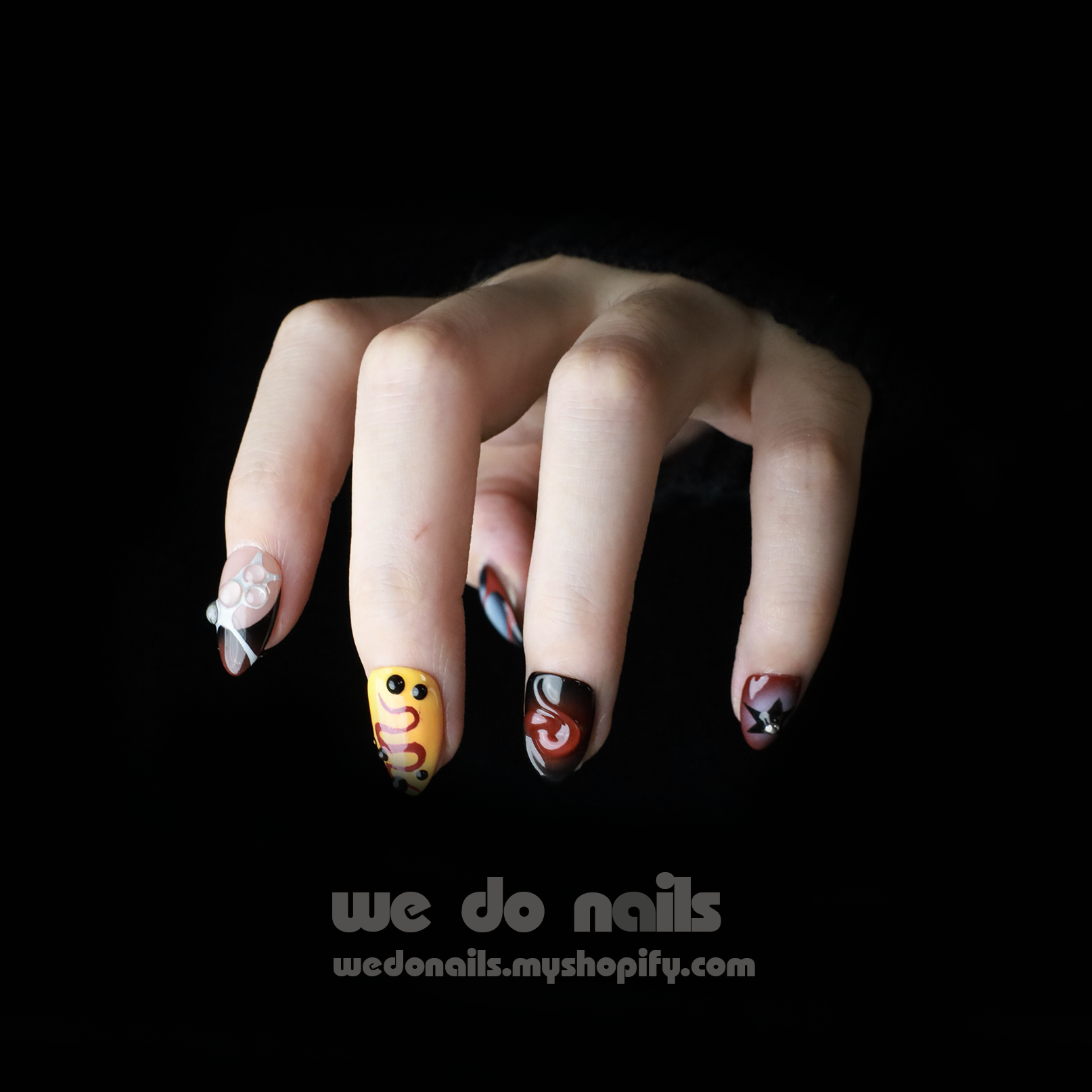 A hand with unique nails against a black background displays colorful designs like smiley faces, abstract patterns, and floral motifs. Text at the bottom reads, Snake-inspired Press-On Nails by We Do Nails – wedonails.myshopify.com.