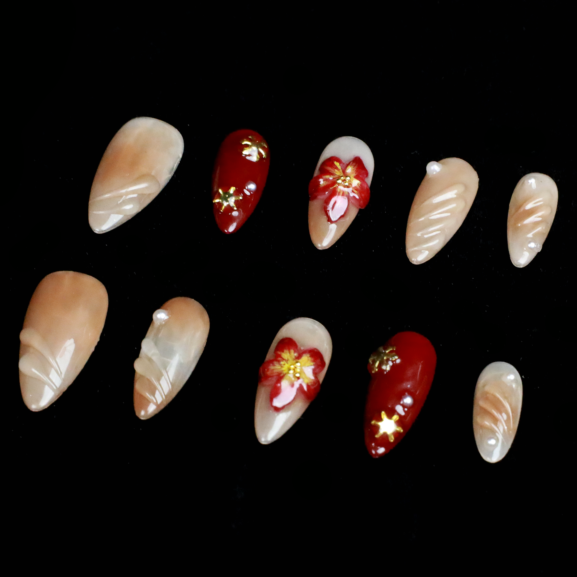 A pair of hands adorned with Elegant Floral Red and Beige Press-On Nails by We Do Nails, featuring intricate red flowers and pearl-gold accents, holds a large black mug. The elongated, almond-shaped nails boast a glossy finish with 3D floral designs against the black background.