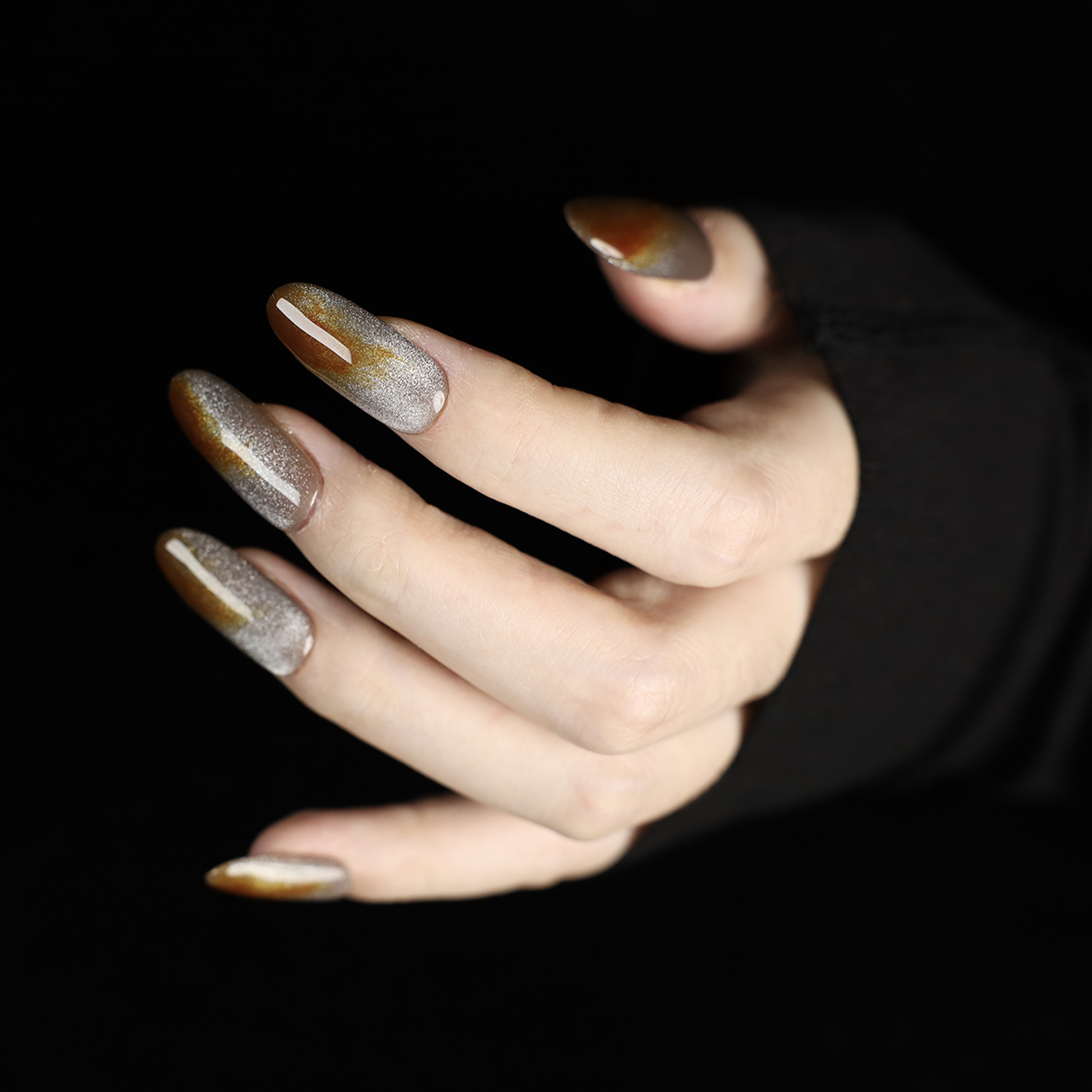 A hand with We Do Nails Elegant Brown Marble Press-On Nails, featuring a subtle metallic chrome accent, holds a simple white mug against a black backdrop.