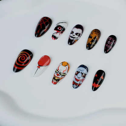 A close-up of two hands shows off the eerie Spooky Nightmares Halloween Press-On Nails by We Do Nails, featuring hand-painted designs like clowns, a pumpkin, and abstract art on a black background while holding a large white mug.