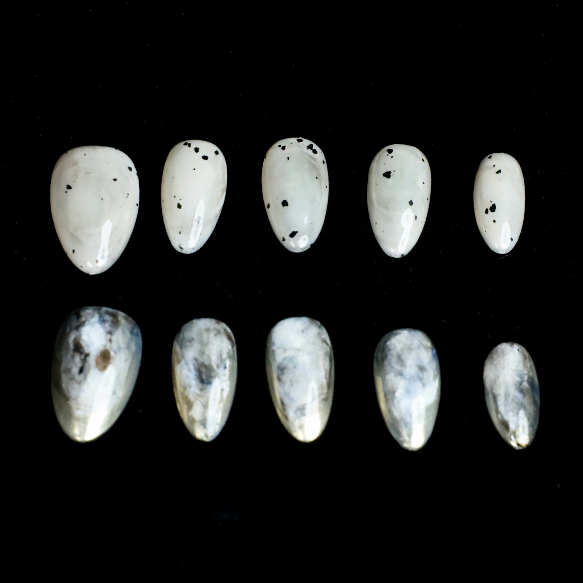 Hands showcasing We Do Nails Marble and Speckled Press On Nails, almond-shaped with a high-gloss shine and scattered speckles, perfectly highlighted against a solid black background.