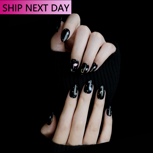 Hands feature We Do Nails Galactic Night Sky Press On Nails with black nails adorned in colorful crescent and star designs, creating a celestial theme. A SHIP NEXT DAY label in a pink rectangle sits at the top left.