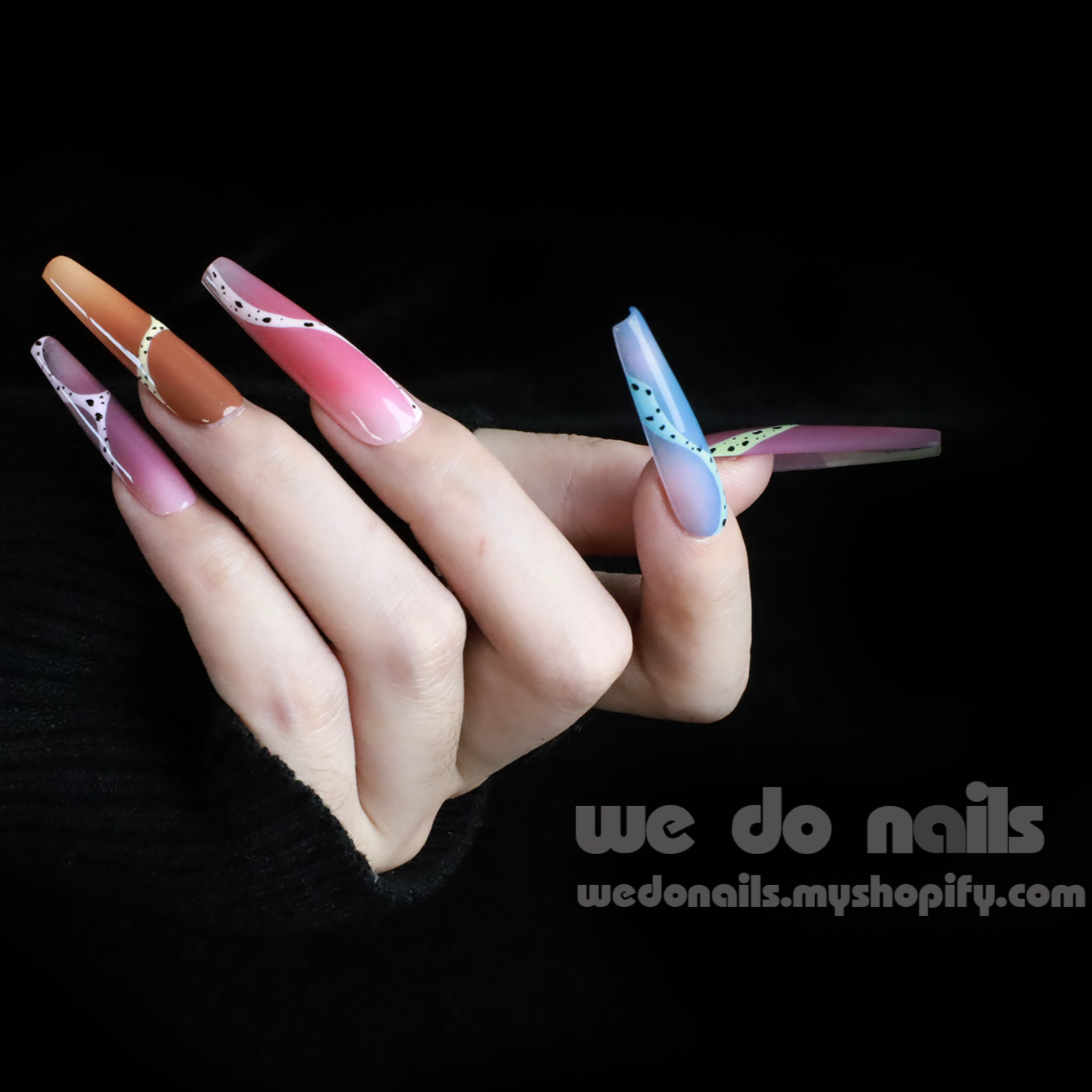 A hand adorned with Milky Rainbow Press-On Nails exhibits a smooth gradient and dotted 3D designs against a black background. The text We Do Nails appears alongside the website link, emphasizing the brands artistry.
