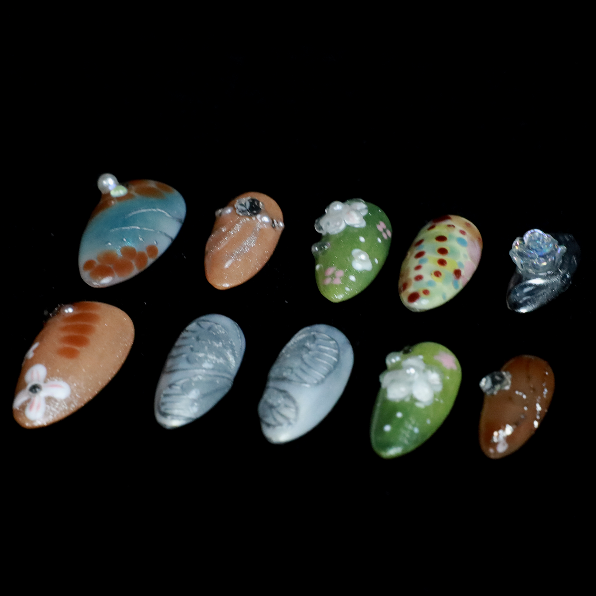 A hand showcases the Fantasy Garden Press-On Nails by We Do Nails against a black background. The nails feature designs of a koi fish with a pearl, peach with rhinestones, 3D green flowers, green with red floral dots, and metallic silver with a crystal accent.