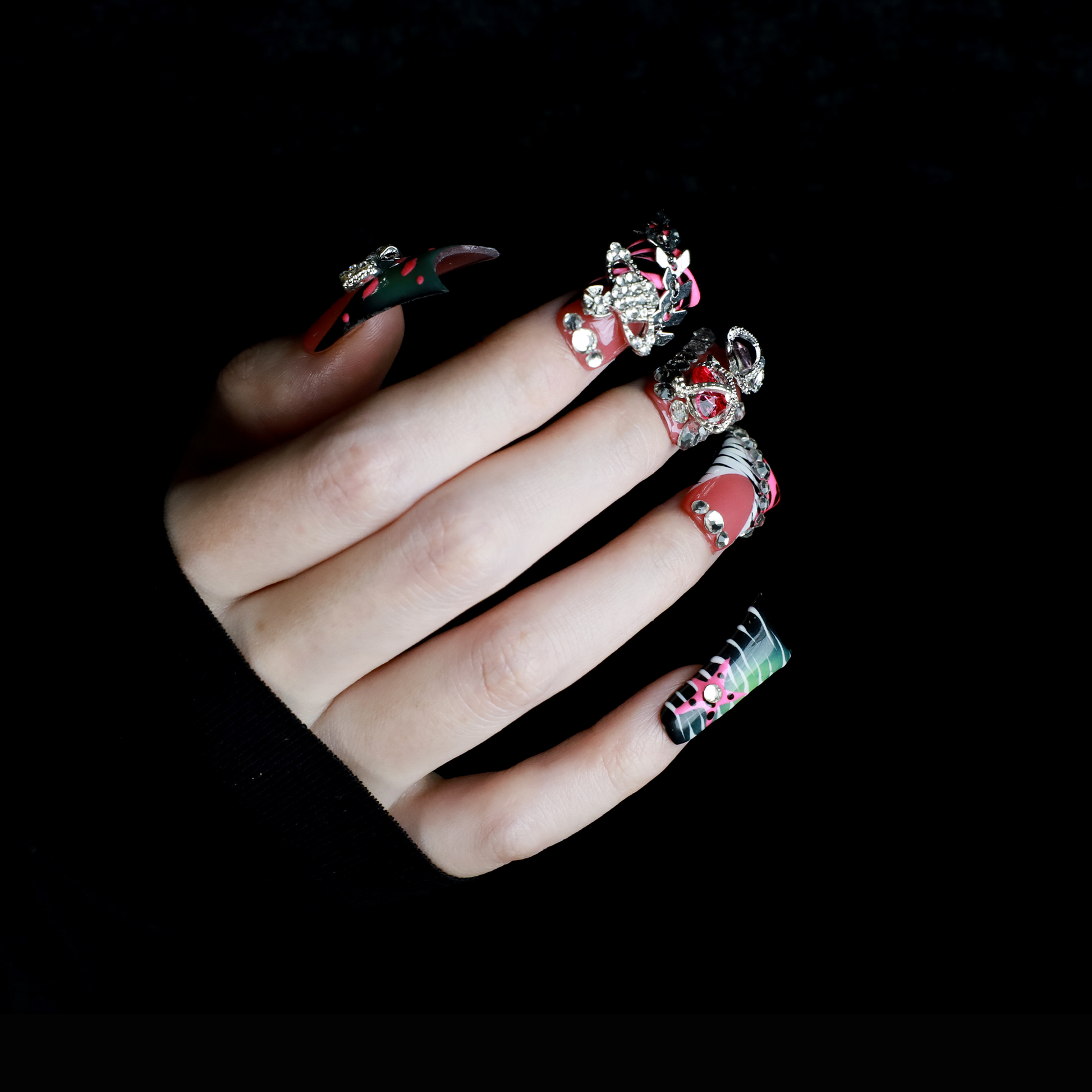 A hand displays Glam Jungle Luxe 3D Long Duck Press-On Nails by We Do Nails, featuring ornate black and red designs with rhinestone gemstones and skulls. The words SHIP NEXT DAY appear in the top-left corner, highlighting their gothic style against a dark background.