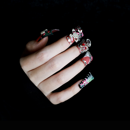A hand displays Glam Jungle Luxe 3D Long Duck Press-On Nails by We Do Nails, featuring ornate black and red designs with rhinestone gemstones and skulls. The words SHIP NEXT DAY appear in the top-left corner, highlighting their gothic style against a dark background.