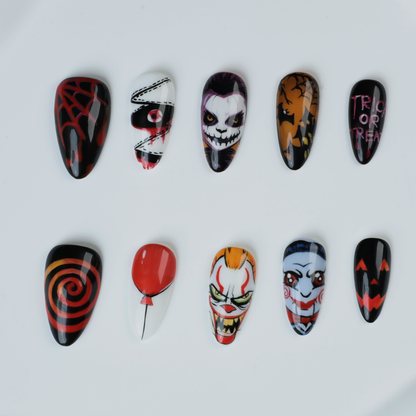 A close-up of two hands shows off the eerie Spooky Nightmares Halloween Press-On Nails by We Do Nails, featuring hand-painted designs like clowns, a pumpkin, and abstract art on a black background while holding a large white mug.