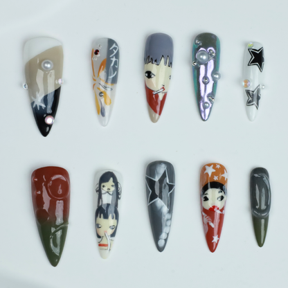 A hand with long, pointed Japanese-Inspired Artistic Press-On Nails by We Do Nails showcases camo patterns in green, red, and gray. Combining kawaii aesthetic and artistic motifs that suggest anime nail art, the hand is partially covered by a black sleeve.