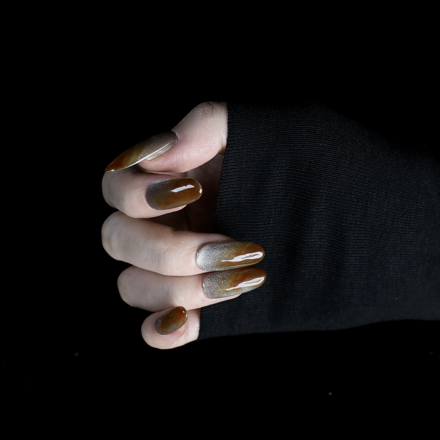 A hand with We Do Nails Elegant Brown Marble Press-On Nails, featuring a subtle metallic chrome accent, holds a simple white mug against a black backdrop.