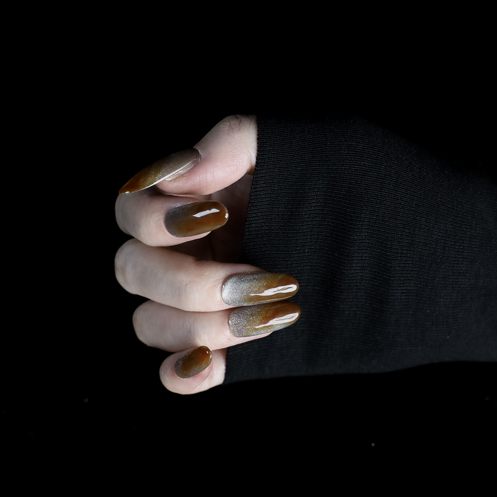 A hand with We Do Nails Elegant Brown Marble Press-On Nails, featuring a subtle metallic chrome accent, holds a simple white mug against a black backdrop.