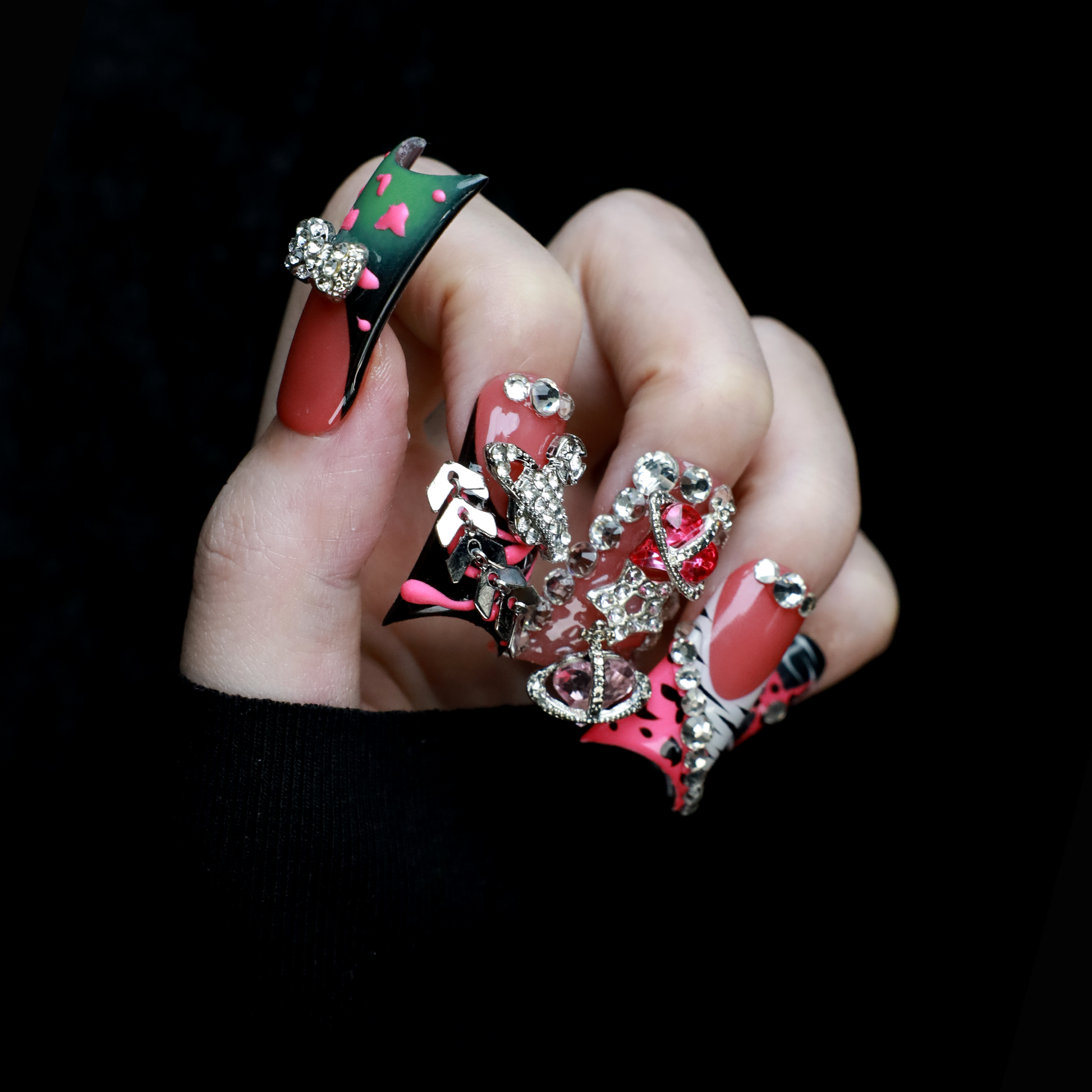 A hand displays Glam Jungle Luxe 3D Long Duck Press-On Nails by We Do Nails, featuring ornate black and red designs with rhinestone gemstones and skulls. The words SHIP NEXT DAY appear in the top-left corner, highlighting their gothic style against a dark background.