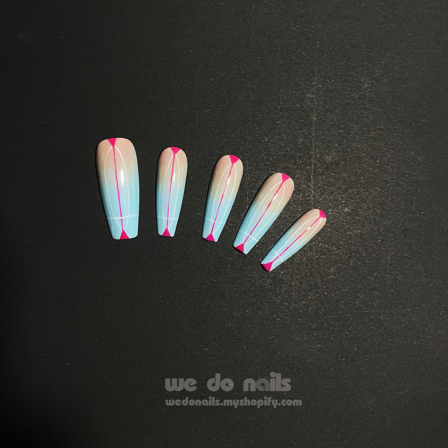 Close-up of hands with long, stiletto-shaped Sky Dream Press-On Nails by We Do Nails, featuring a glossy pastel blue with pink tips. A silver ring with a pearl graces one finger against a dark, striped fabric backdrop that enhances the elegant style.
