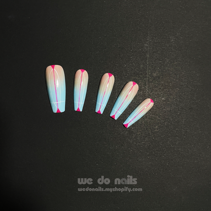 Close-up of hands with long, stiletto-shaped Sky Dream Press-On Nails by We Do Nails, featuring a glossy pastel blue with pink tips. A silver ring with a pearl graces one finger against a dark, striped fabric backdrop that enhances the elegant style.